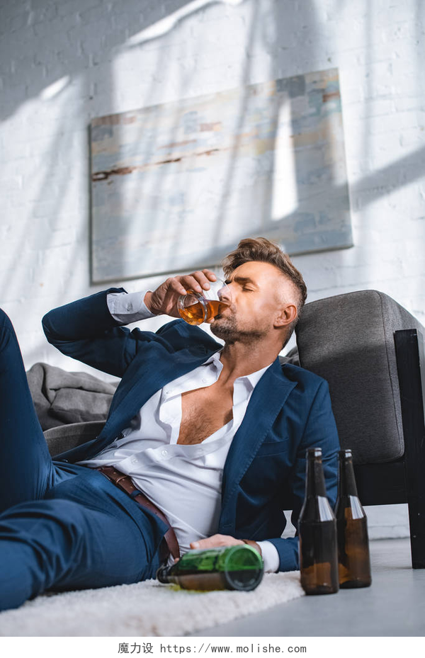 一个伤心的男人躺在地毯上喝着酒抑郁的商人在客厅里的瓶子附近喝威士忌 